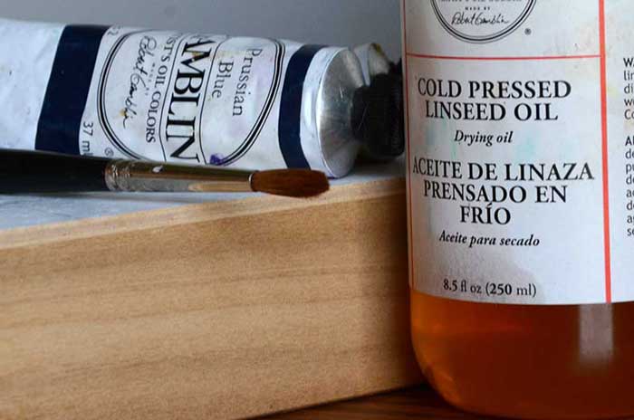 An oil painting panel, a tube of oil paint, and a jar of linseed oil.